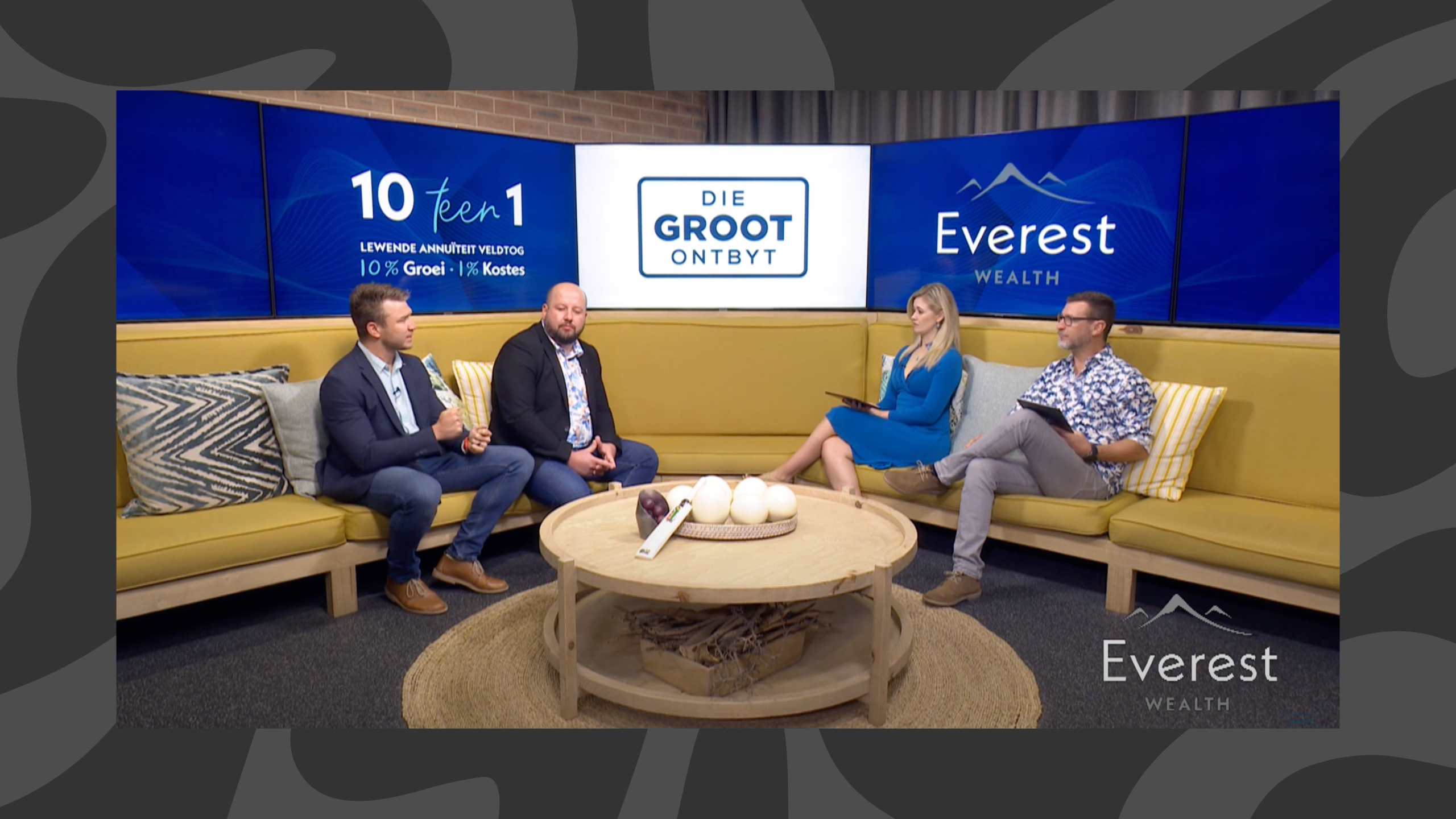 Four people are sitting on yellow couches in a studio set for "Die Groot Ontbyt." Two people appear to interview two others, with blue branding in the background.